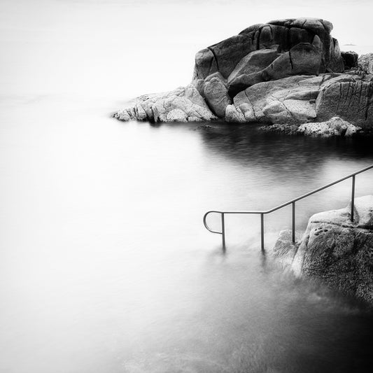 The Descent — iron railing descending into misty long-exposure sea with granite rocks, black and white fine art photography by Roy Fraser
