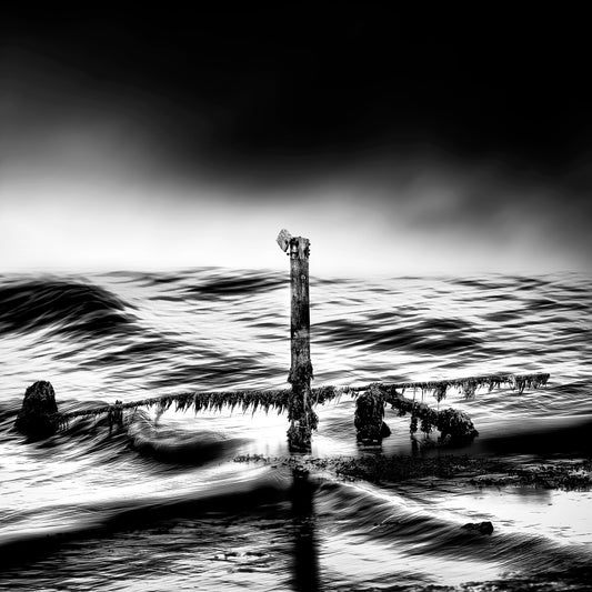 The Last Post — solitary weathered jetty post draped in seaweed in churning swirling sea under a dramatic dark sky, black and white fine art photography by Roy Fraser