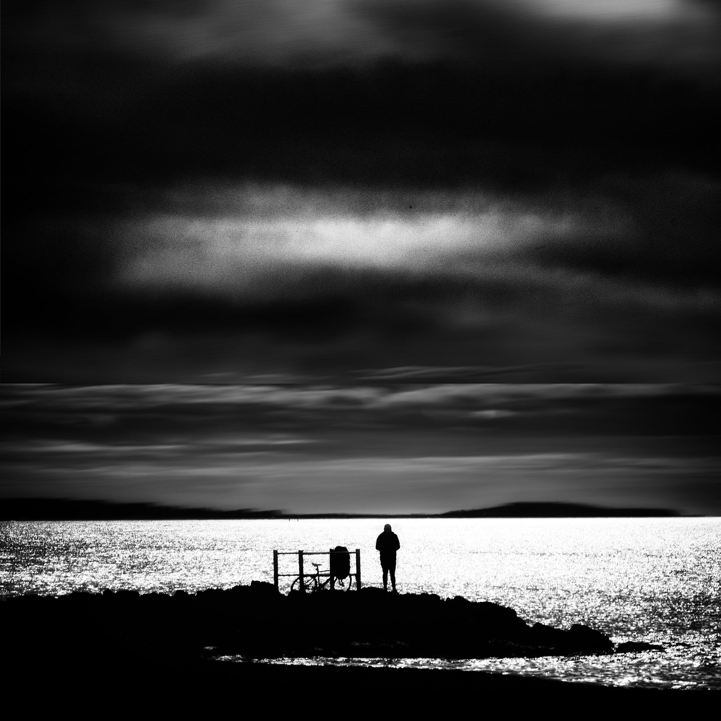 Chinmoku — two figures silhouetted on a dark rocky headland against a stormy sky, black and white fine art photography
