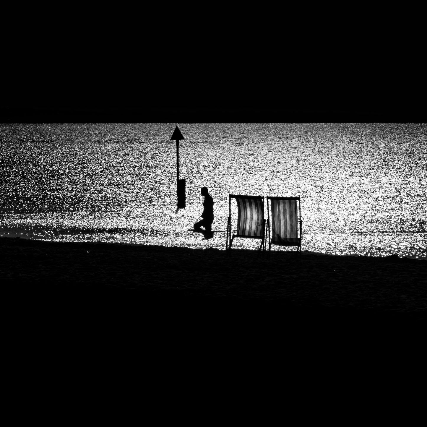 Deckchair Passage — two empty deckchairs on dark shore with jet ski on glittering silver sea, black and white fine art photography