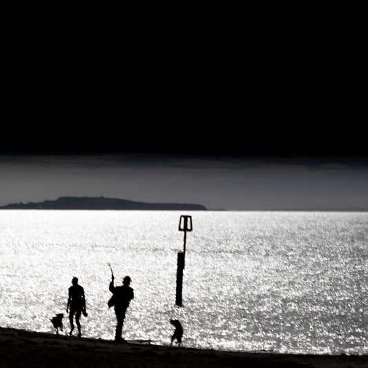 Kazoku no Nagare — family silhouette with dog on glittering shoreline, rectangular beach marker, island on horizon, black and white fine art photography