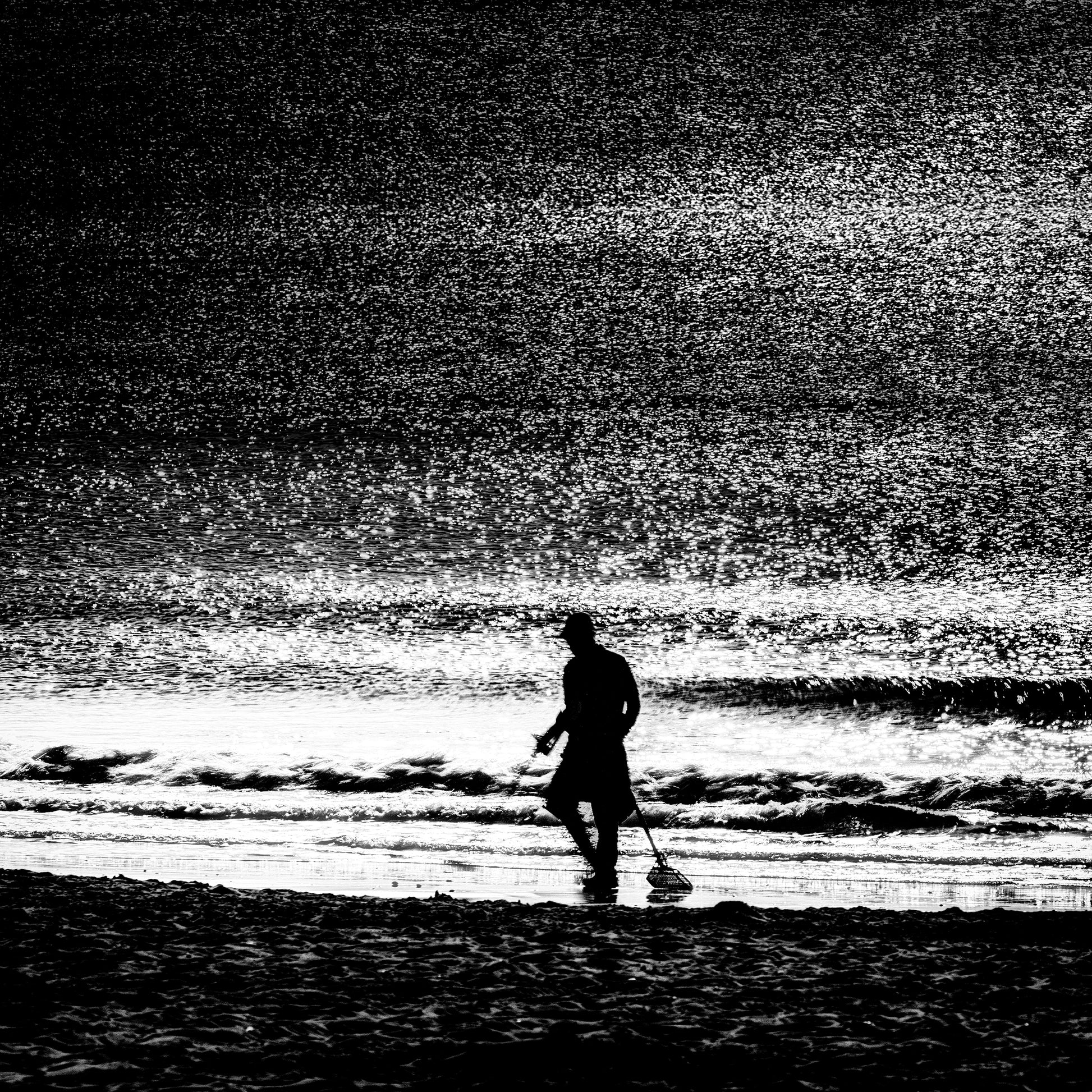 Tansakusha | 探索者 — lone metal detectorist silhouetted against a glittering Dorset shoreline