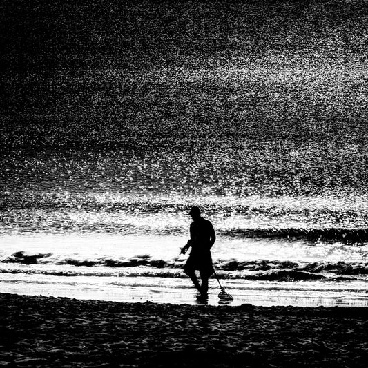 Tansakusha | 探索者 — lone metal detectorist silhouetted against a glittering Dorset shoreline